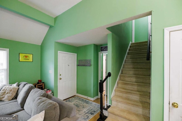 living room featuring stairway, vaulted ceiling with beams, and baseboards