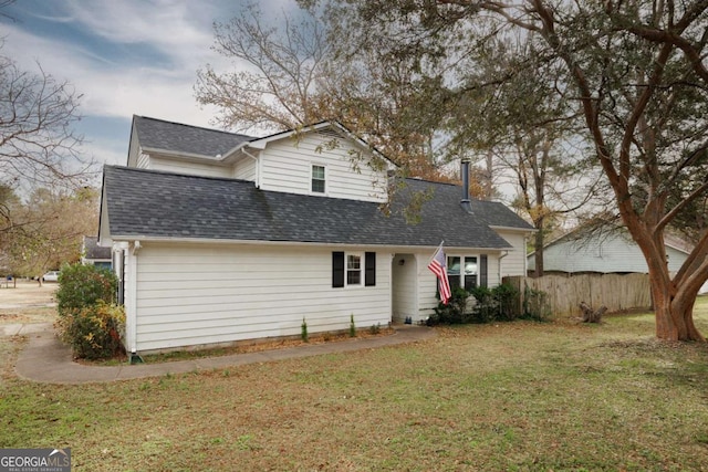 traditional-style house with a front yard, fence, and a shingled roof