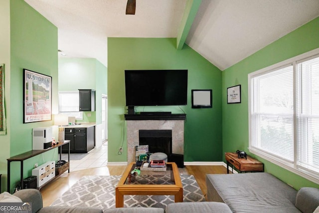 living area featuring ceiling fan, baseboards, lofted ceiling with beams, a premium fireplace, and light wood-style flooring