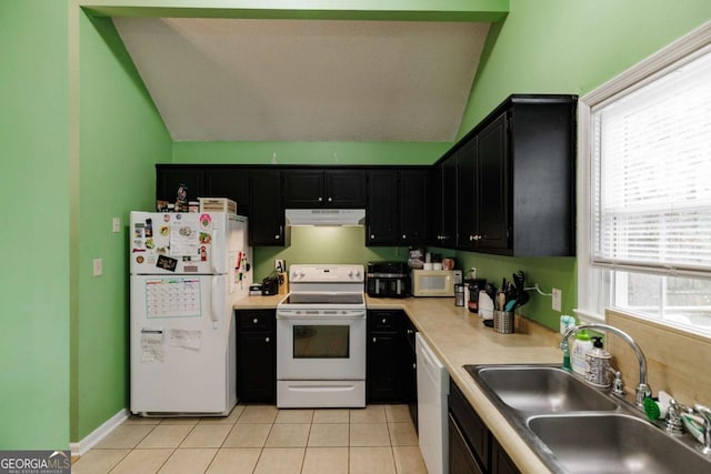 kitchen with under cabinet range hood, light tile patterned floors, dark cabinetry, white appliances, and a sink