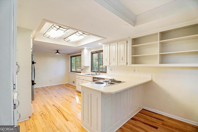 kitchen featuring light wood finished floors, light countertops, stovetop, a peninsula, and a sink