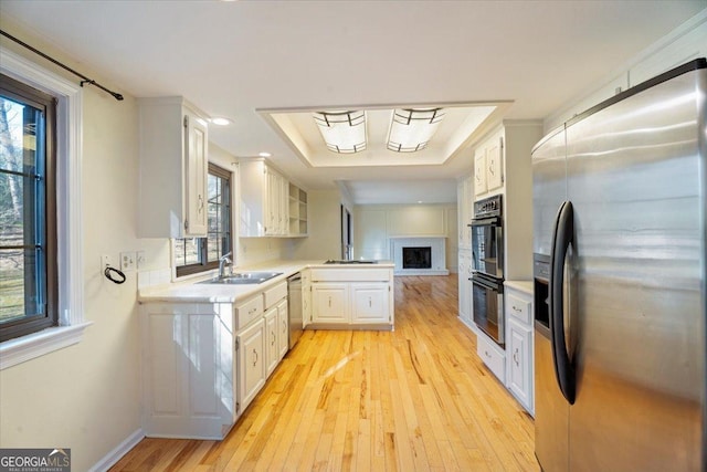 kitchen featuring light countertops, light wood-style flooring, stainless steel appliances, a raised ceiling, and a sink