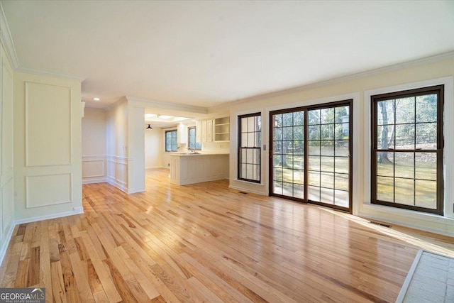 unfurnished living room with light wood finished floors, visible vents, a decorative wall, and ornamental molding