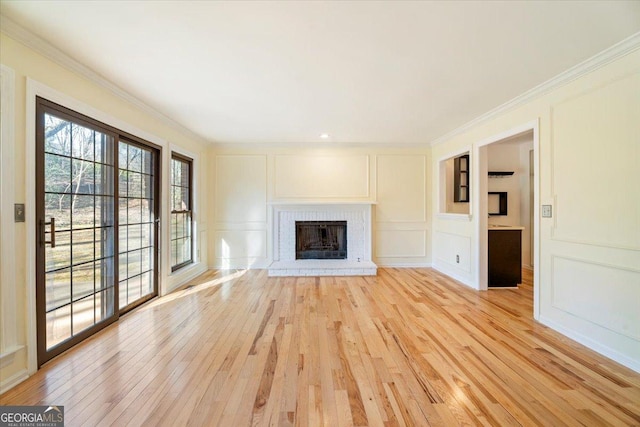 unfurnished living room featuring crown molding, a decorative wall, a fireplace, and light wood finished floors