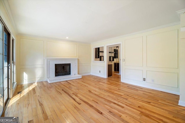 unfurnished living room featuring a fireplace, a decorative wall, light wood-style flooring, and ornamental molding