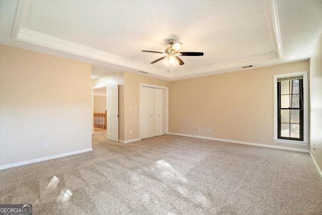 carpeted spare room with visible vents, crown molding, baseboards, a tray ceiling, and a ceiling fan