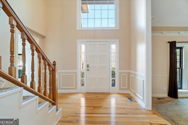 entrance foyer featuring visible vents, light wood-style flooring, stairs, and a decorative wall