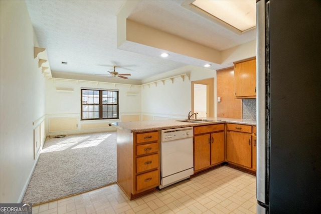 kitchen featuring dishwasher, light countertops, a peninsula, freestanding refrigerator, and a sink