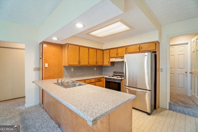 kitchen featuring a sink, under cabinet range hood, range with gas stovetop, freestanding refrigerator, and a peninsula