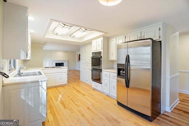 kitchen featuring dobule oven black, light countertops, stainless steel refrigerator with ice dispenser, and a sink