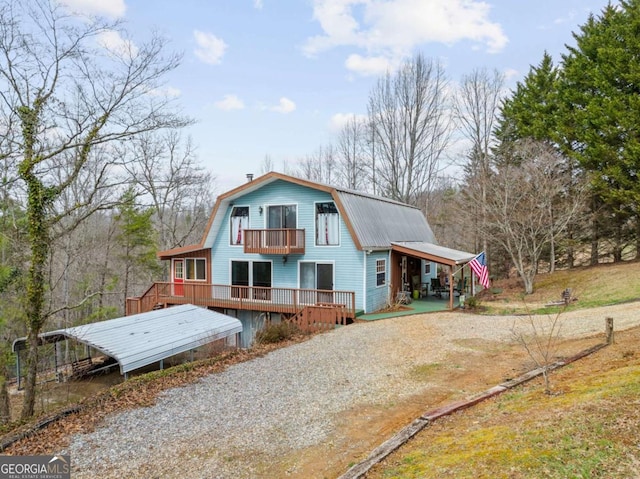 back of property featuring a gambrel roof, driveway, a balcony, metal roof, and an attached carport