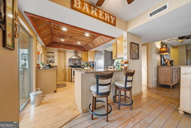 kitchen with a ceiling fan, visible vents, light wood finished floors, appliances with stainless steel finishes, and wall chimney range hood