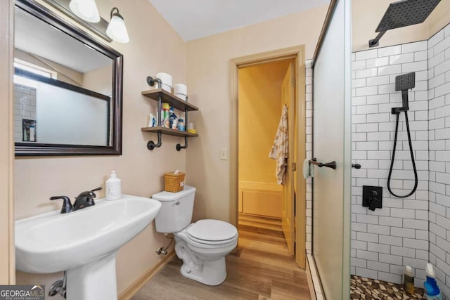 bathroom featuring a sink, toilet, wood finished floors, and a tile shower