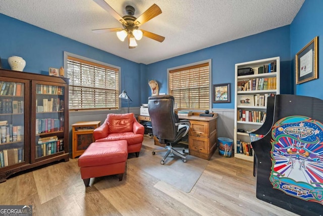 office space featuring a ceiling fan, a textured ceiling, wood finished floors, and wainscoting