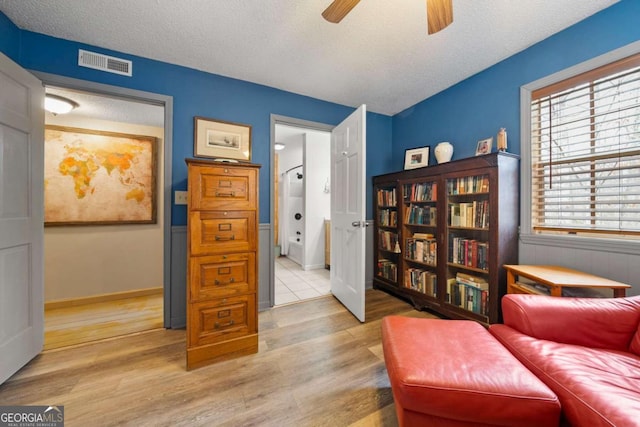 sitting room with visible vents, baseboards, ceiling fan, light wood-style flooring, and a textured ceiling