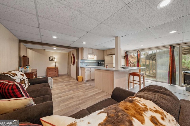 living area with light wood finished floors, a paneled ceiling, recessed lighting, and a wealth of natural light