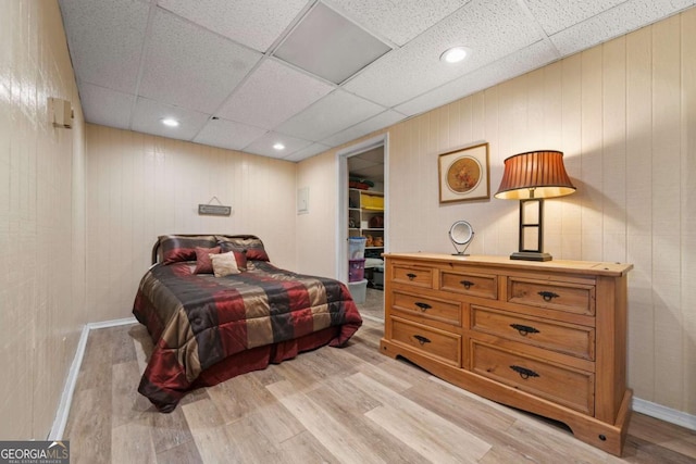 bedroom featuring a spacious closet, baseboards, light wood-style flooring, a closet, and a paneled ceiling