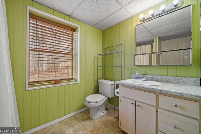 full bath featuring vanity, a drop ceiling, tile patterned flooring, wood walls, and toilet