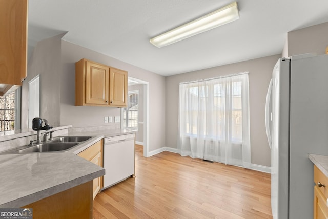 kitchen with light brown cabinets, baseboards, light wood-style floors, white appliances, and a sink