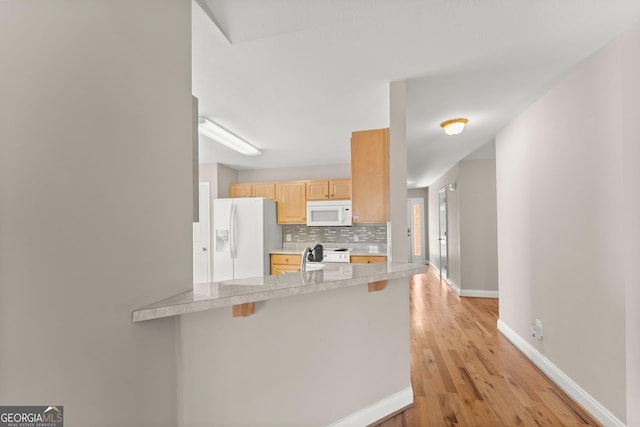 kitchen with tasteful backsplash, light brown cabinets, light countertops, a peninsula, and white appliances