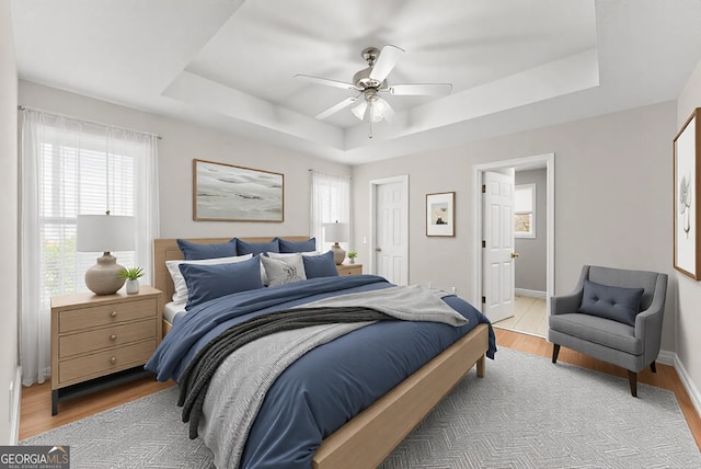 bedroom featuring a tray ceiling, light wood-style flooring, a ceiling fan, and baseboards