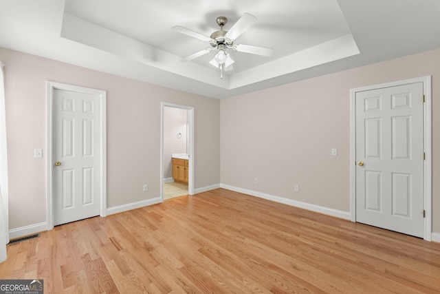 unfurnished bedroom featuring light wood finished floors, visible vents, a raised ceiling, and baseboards