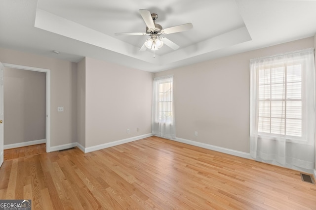 spare room featuring a tray ceiling, light wood-style floors, visible vents, and baseboards