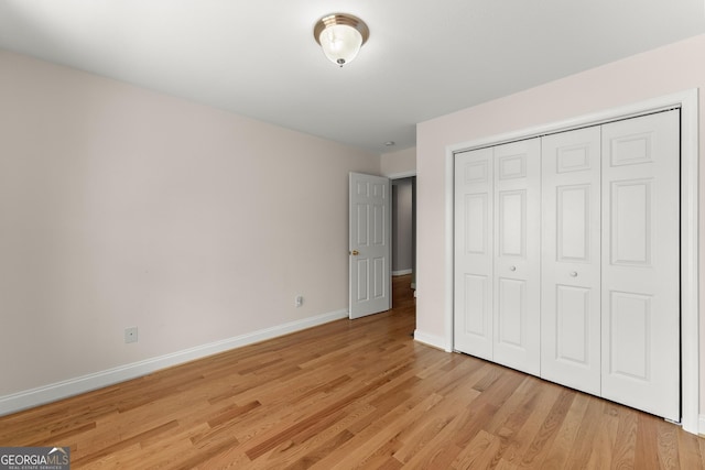 unfurnished bedroom featuring baseboards, light wood-type flooring, and a closet