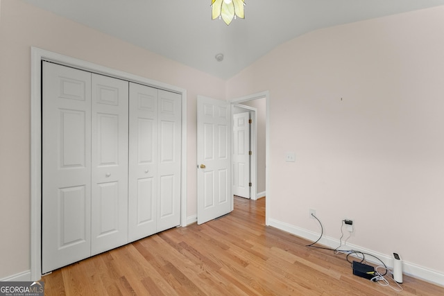 unfurnished bedroom featuring light wood-type flooring, baseboards, a closet, and vaulted ceiling