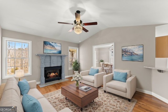 living area with baseboards, light wood finished floors, a fireplace with flush hearth, ceiling fan, and vaulted ceiling