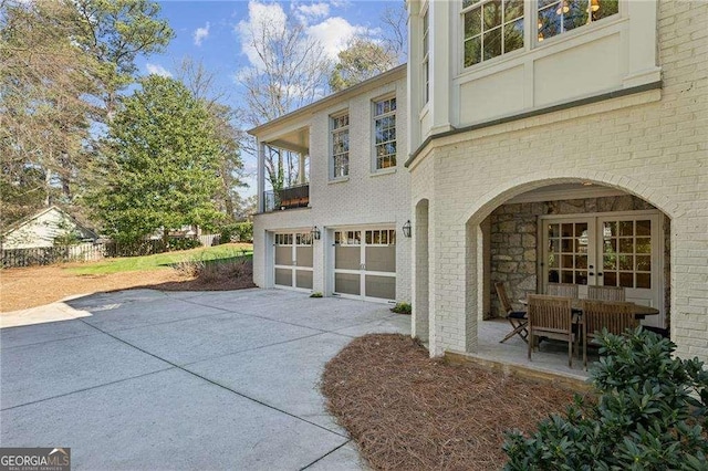 exterior space featuring brick siding, french doors, a balcony, a garage, and driveway