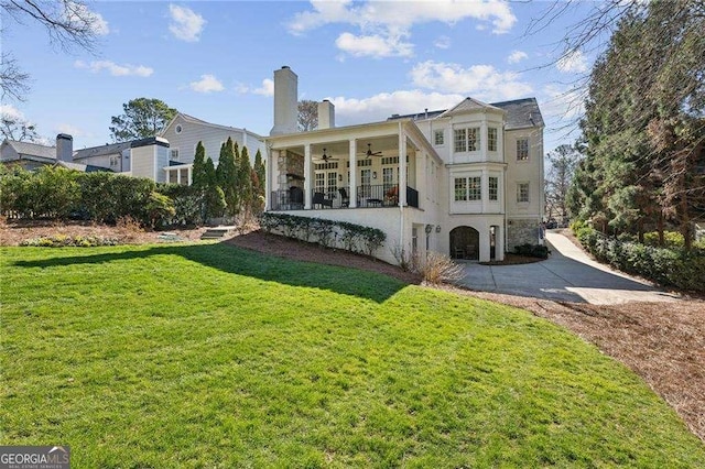 rear view of house with ceiling fan, stucco siding, a chimney, a yard, and driveway