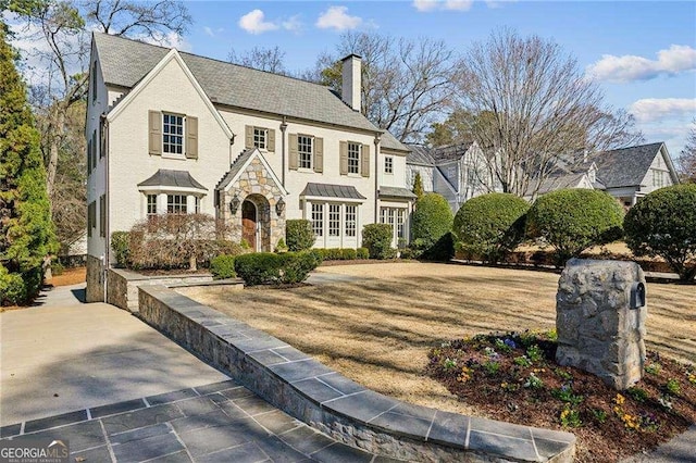 english style home featuring stone siding and a chimney