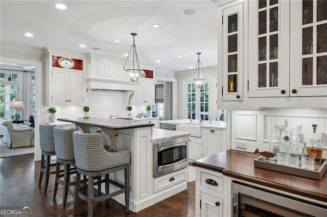 kitchen featuring stainless steel microwave, a kitchen island, ornamental molding, and white cabinetry