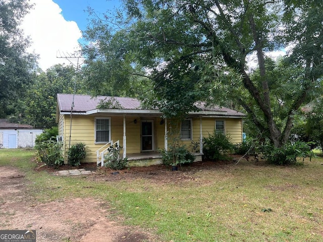 ranch-style house featuring covered porch, metal roof, and a front yard