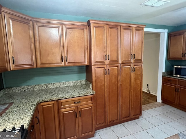 kitchen featuring stainless steel microwave, visible vents, and brown cabinetry