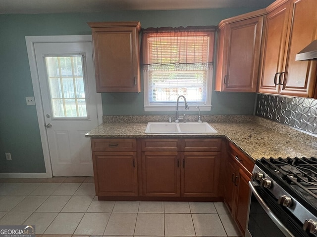 kitchen featuring light tile patterned flooring, gas stove, brown cabinetry, and a sink