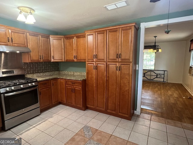 kitchen with light tile patterned flooring, brown cabinetry, under cabinet range hood, and stainless steel range with gas cooktop