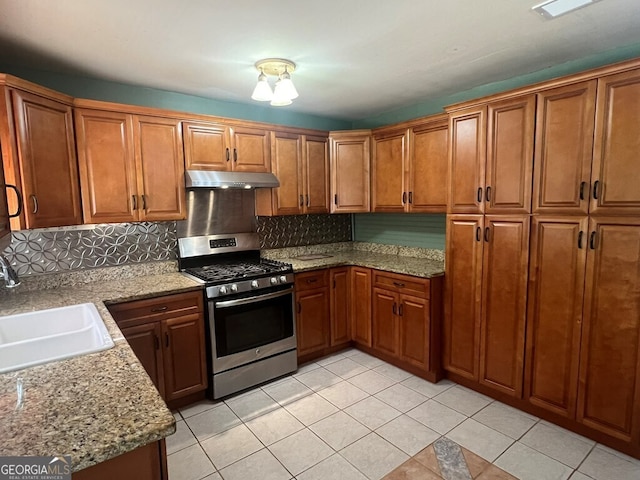 kitchen featuring gas stove, under cabinet range hood, brown cabinetry, and a sink