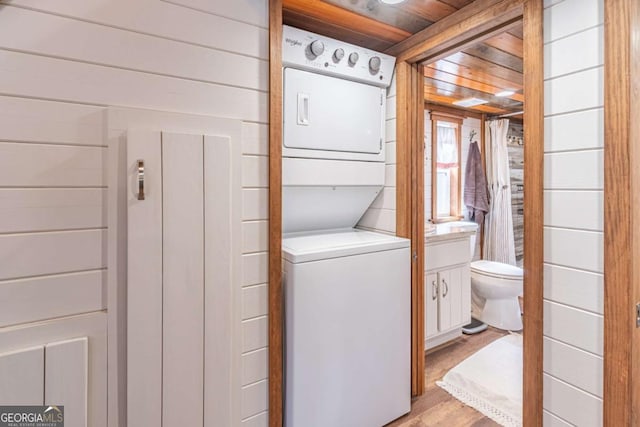 washroom featuring light wood finished floors, laundry area, stacked washing maching and dryer, and wooden walls