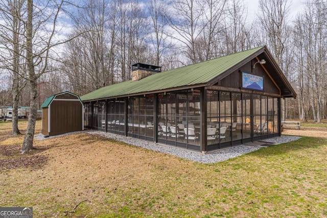 view of property exterior featuring an outbuilding, a shed, a chimney, a lawn, and metal roof