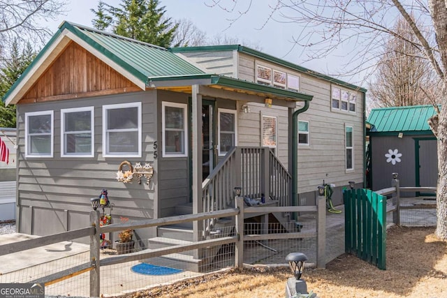 view of front facade with a storage shed, an outdoor structure, fence, and metal roof