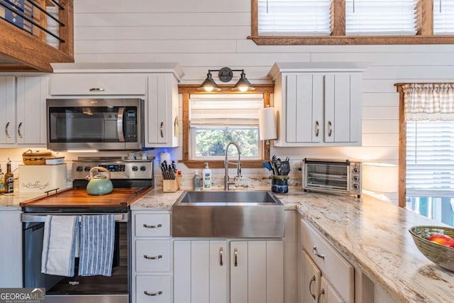 kitchen with light stone counters, a toaster, a sink, stainless steel appliances, and white cabinets