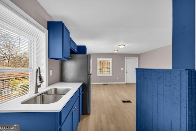 kitchen featuring light wood finished floors, visible vents, blue cabinetry, light countertops, and a sink