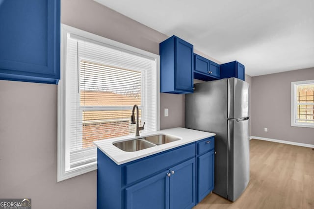 kitchen featuring a sink, blue cabinetry, light countertops, and freestanding refrigerator