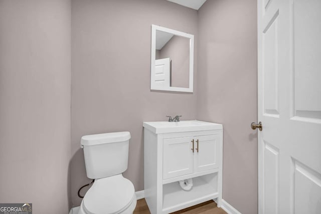 half bath featuring toilet, vanity, baseboards, and wood finished floors