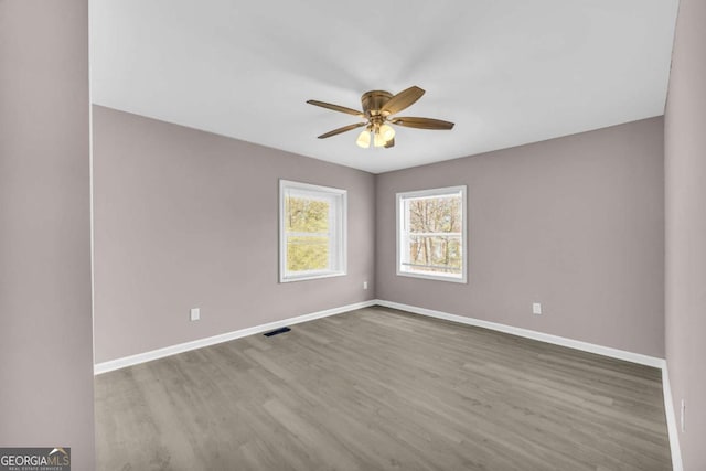 empty room with a ceiling fan, visible vents, wood finished floors, and baseboards