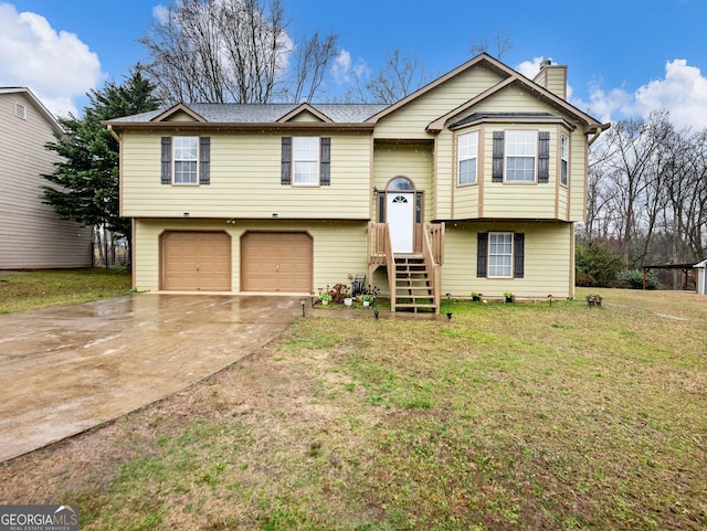 raised ranch featuring a front lawn, an attached garage, driveway, and a chimney