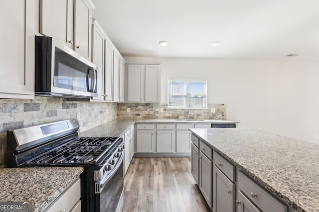 7783 Hansel Ln, Lithonia, GA 30058 - kitchen with appliances with stainless steel finishes, light wood-type flooring, a sink, decorative backsplash, and light stone counters