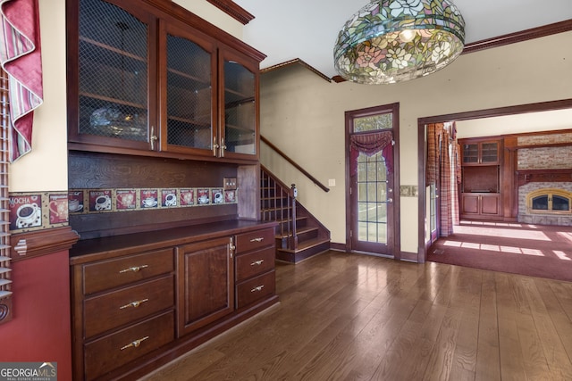 interior space featuring a fireplace with raised hearth, crown molding, baseboards, stairs, and dark wood-style flooring